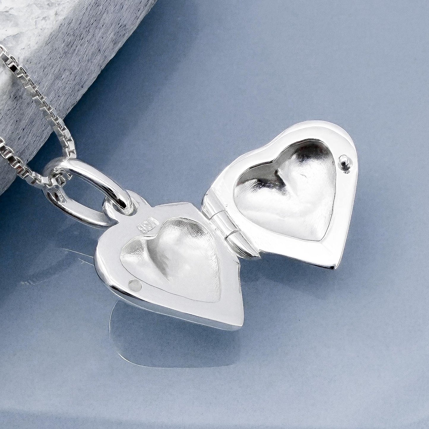 A silver heart-shaped locket with a chain attached, open to reveal a heart inside.