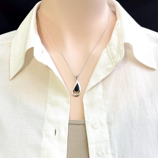 A close-up view of a mannequin wearing a white collared shirt and a silver necklace with a pendant.