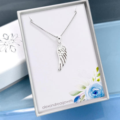 A silver necklace with a wing pendant is displayed in a white box with a floral design.