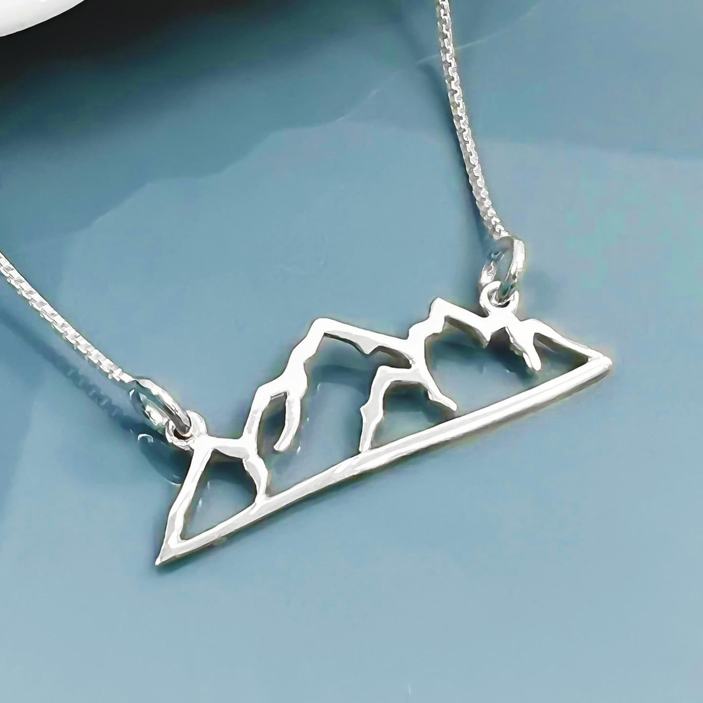A silver necklace with a pendant in the shape of a mountain range.