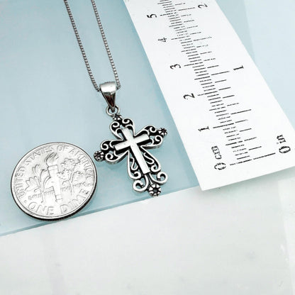 a silver cross pendant hanging from a chain, placed next to a United States one-dollar coin.