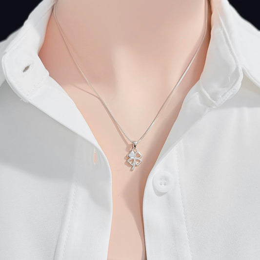 A silver necklace with a small pendant is worn around a person's neck, who is wearing a white collared shirt.