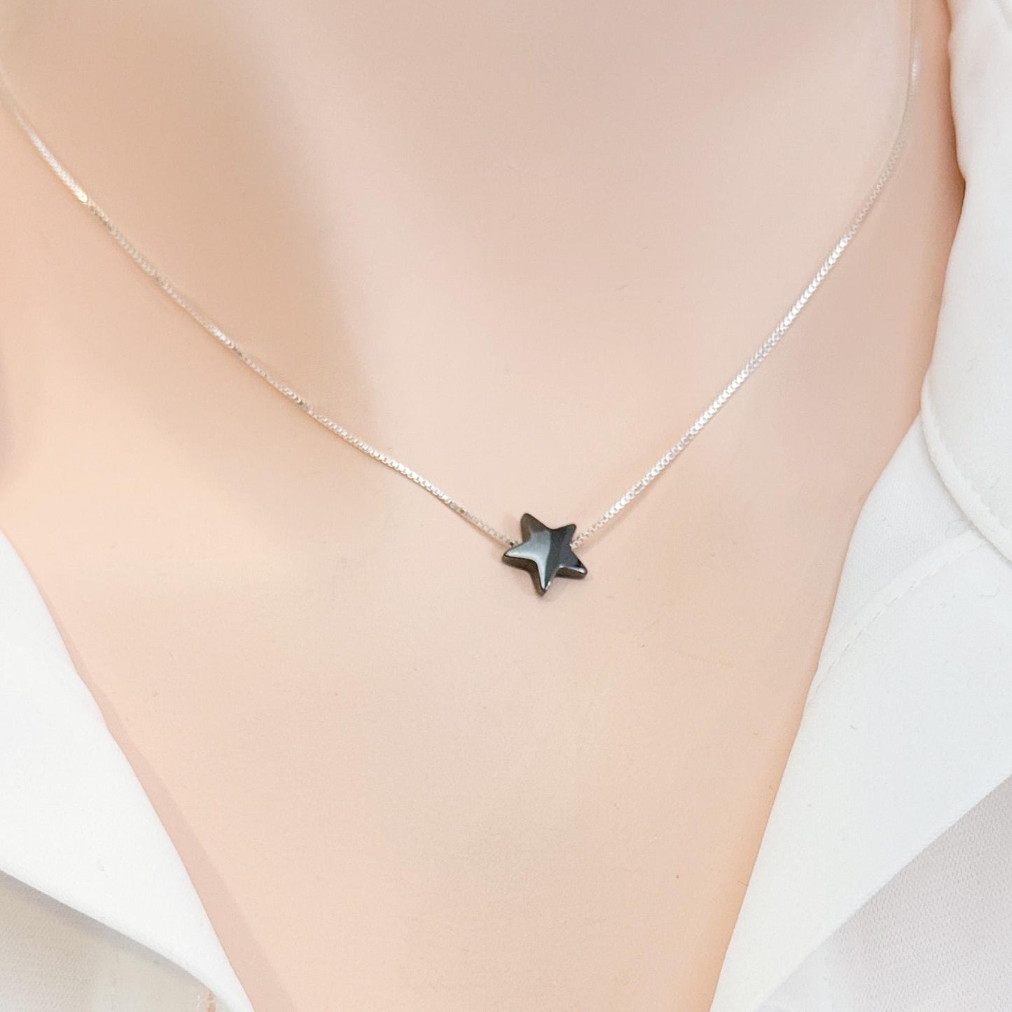 A silver necklace with a small black star pendant is shown on a person's neck.
