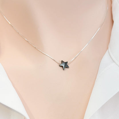 A silver necklace with a small black star pendant is shown on a person's neck.