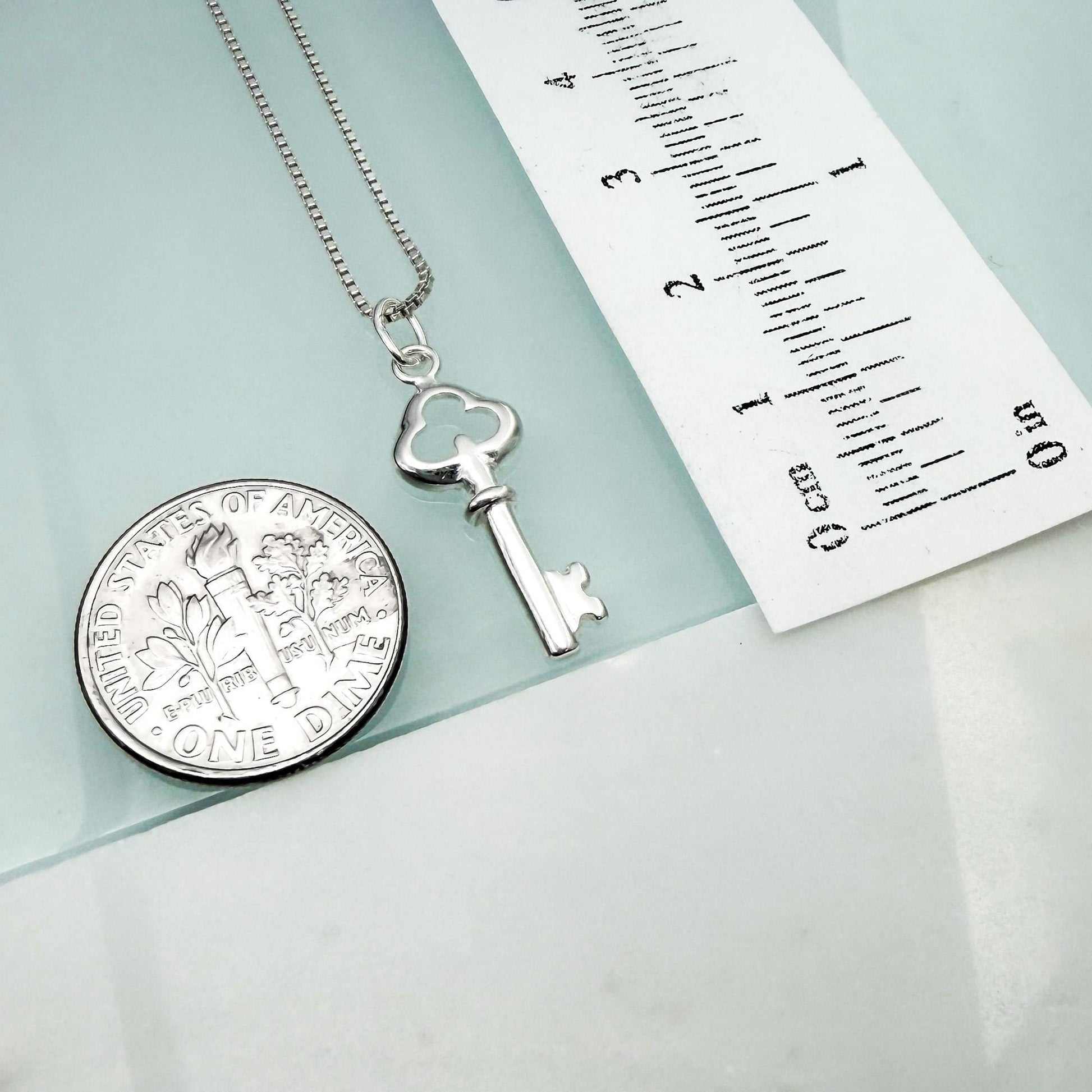 a silver key pendant and a United States one-dollar coin, both placed on a light blue surface.