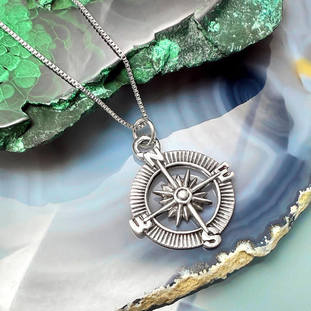 A silver compass pendant with a chain is displayed against a colorful background.