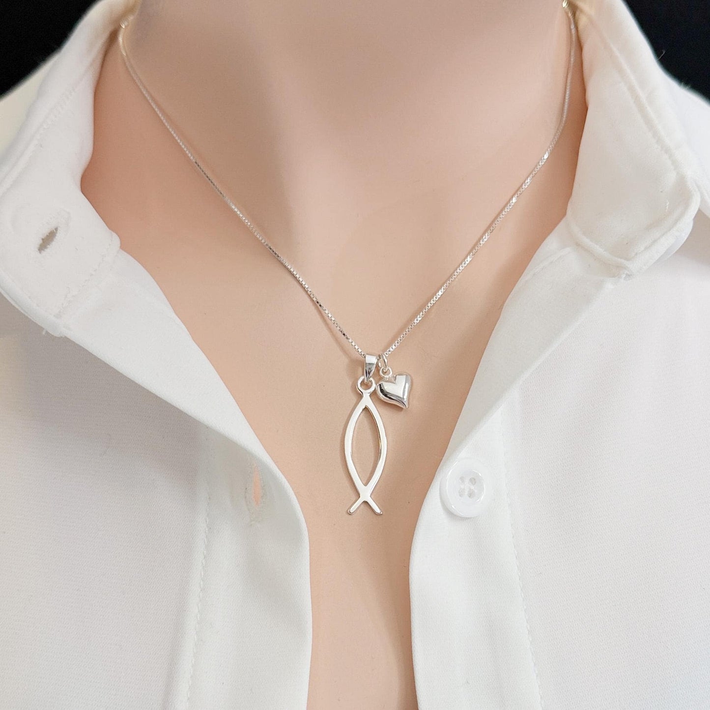 A silver necklace with a pendant featuring a fish design, worn around a person's neck.