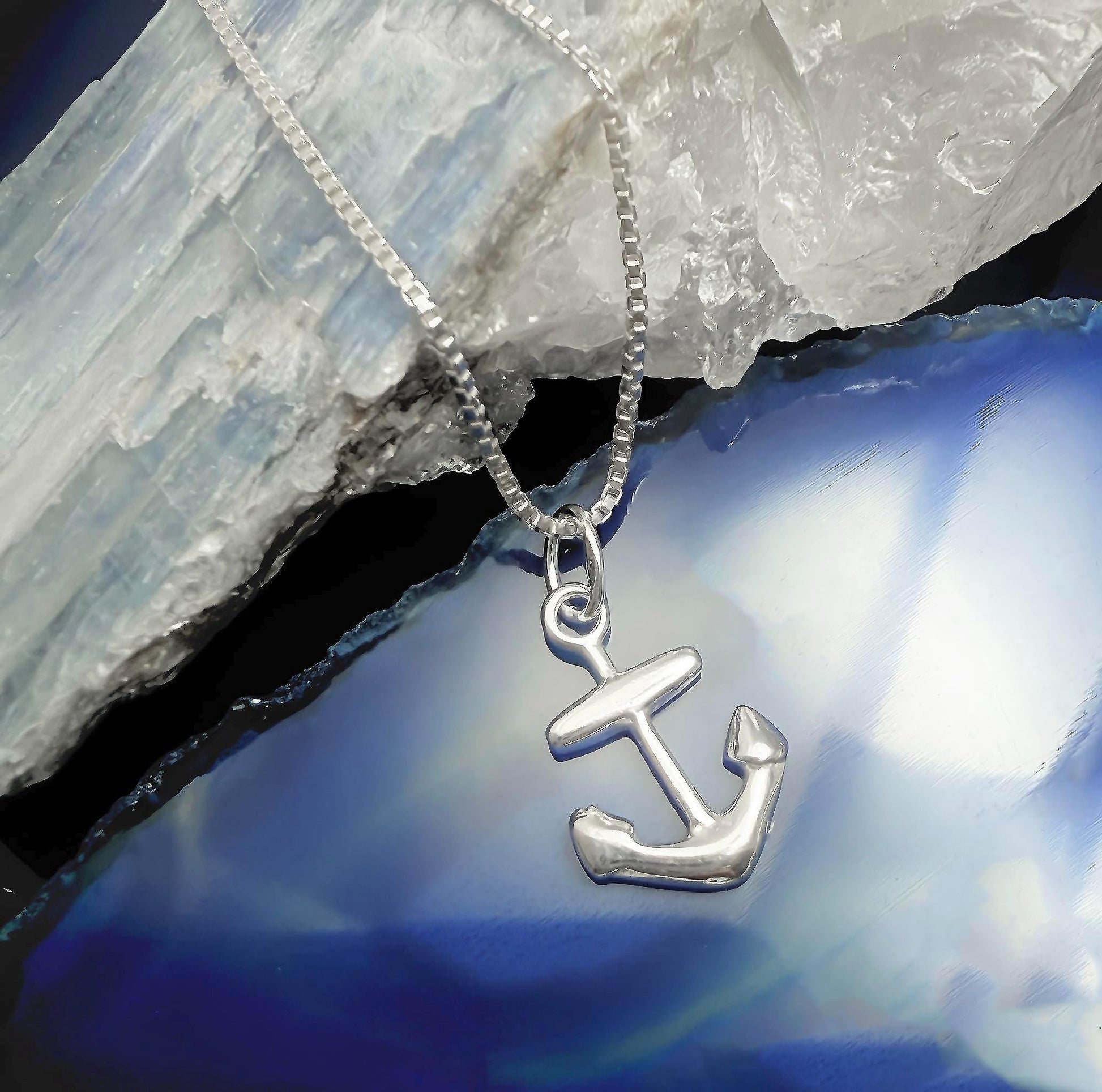 A silver anchor pendant is displayed on a silver chain against a blue background.