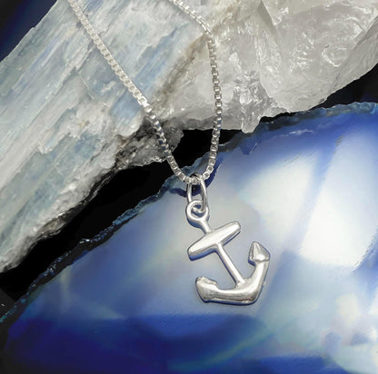A silver anchor pendant is displayed on a silver chain against a blue background.