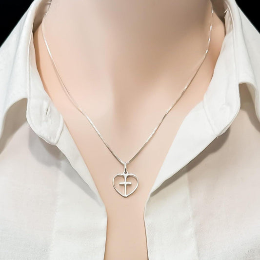 A silver necklace with a heart-shaped pendant is worn around a person's neck, who is wearing a white collared shirt.