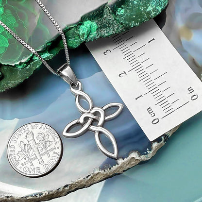 a silver cross pendant with a chain, placed on top of a US quarter, and a ruler for scale.