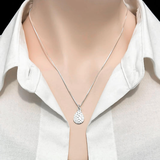 A close-up view of a person wearing a white collared shirt and a silver necklace with a pendant.