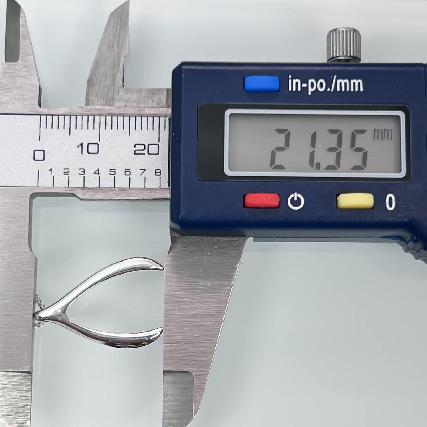 A digital caliper is being used to measure the size of a silver object, which appears to be a piece of jewelry.