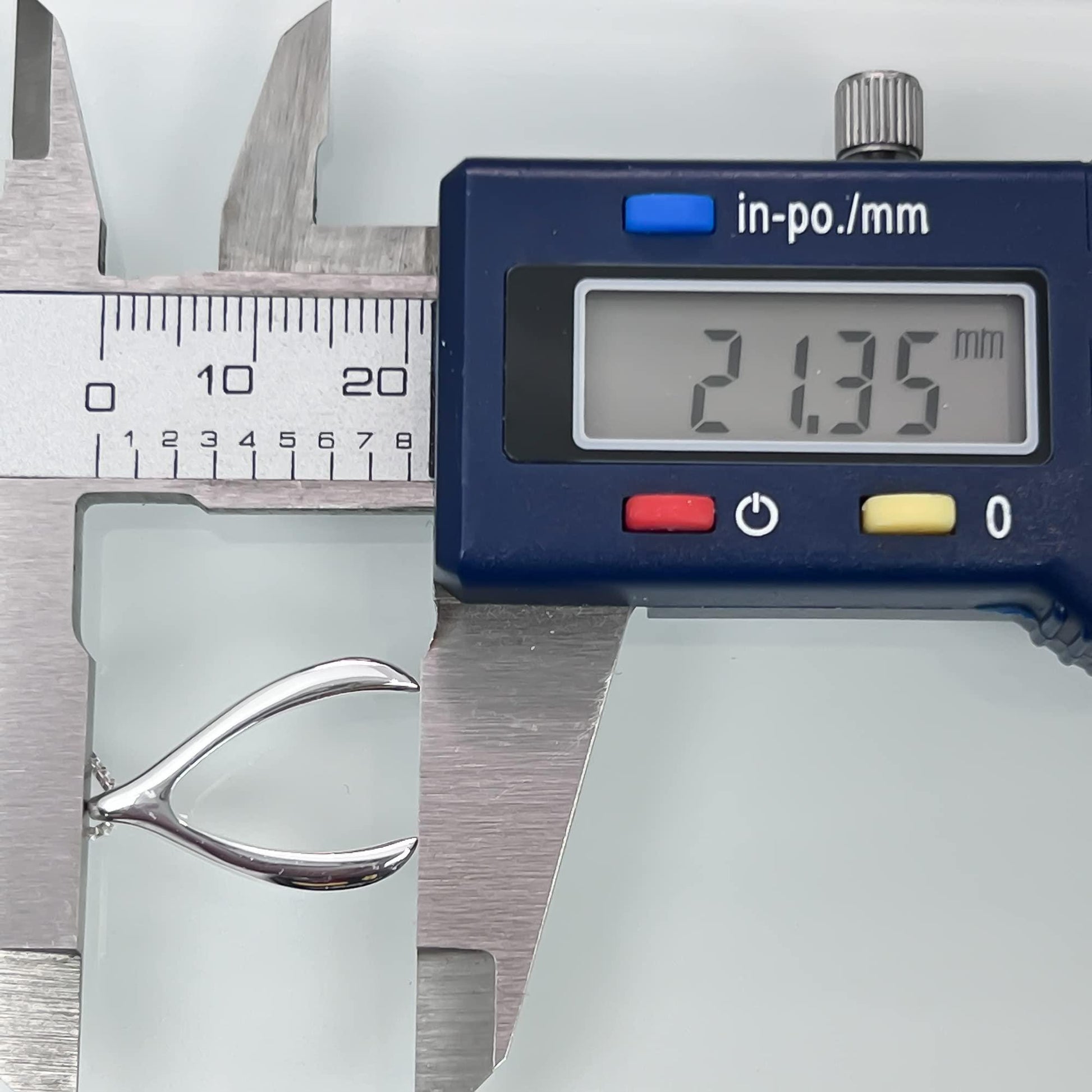 A digital caliper is being used to measure the size of a silver object, which appears to be a piece of jewelry.