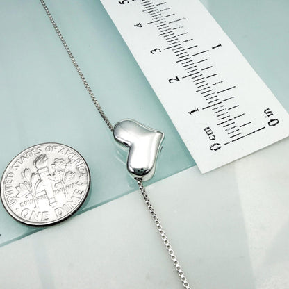 a silver heart-shaped charm attached to a chain, with a United States one-dollar coin placed next to it.