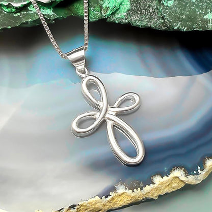 A silver cross pendant with a twisted design is displayed on a chain against a blue and green background.