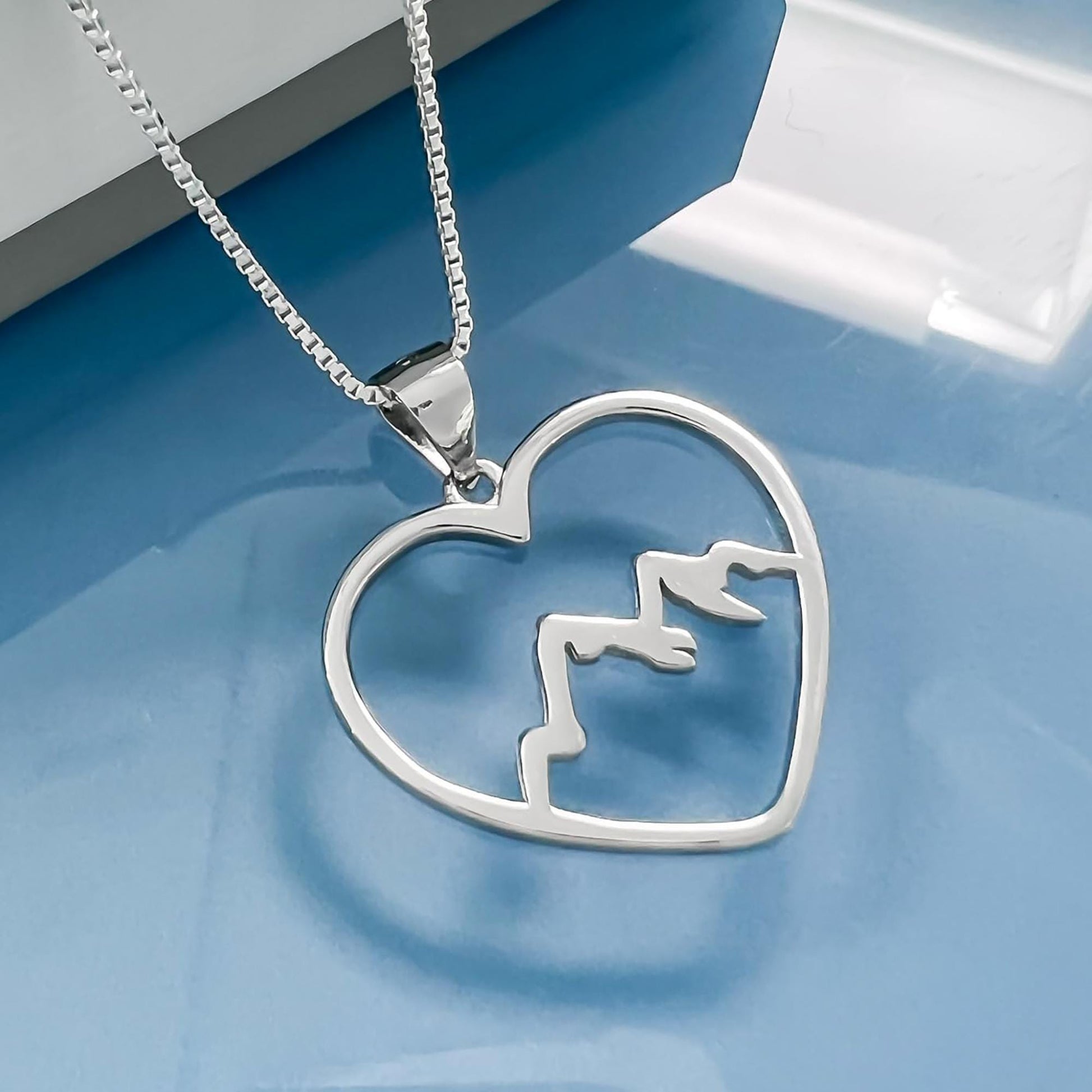 A silver heart-shaped pendant with mountain silhouettes on it, hanging from a chain.