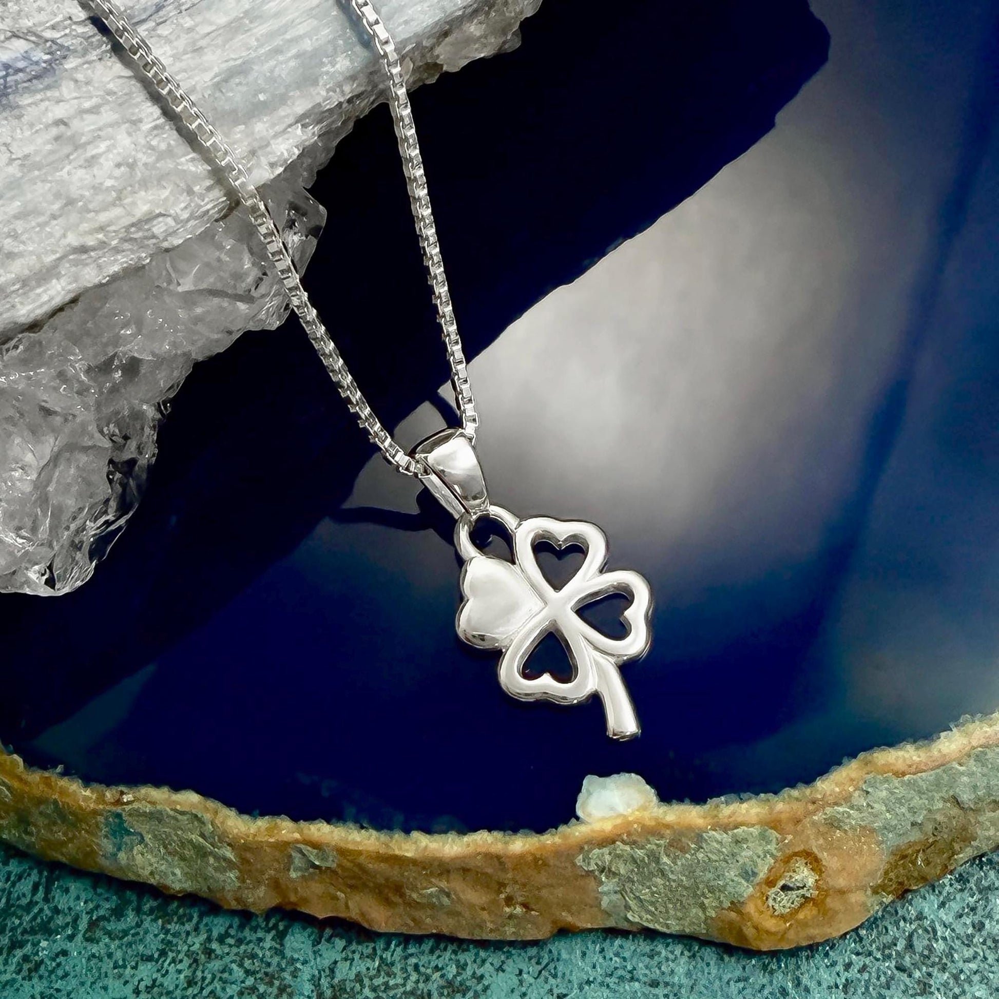 A silver-colored pendant featuring a four-leaf clover design is displayed on a chain against a blue background.