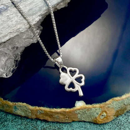 A silver-colored pendant featuring a four-leaf clover design is displayed on a chain against a blue background.