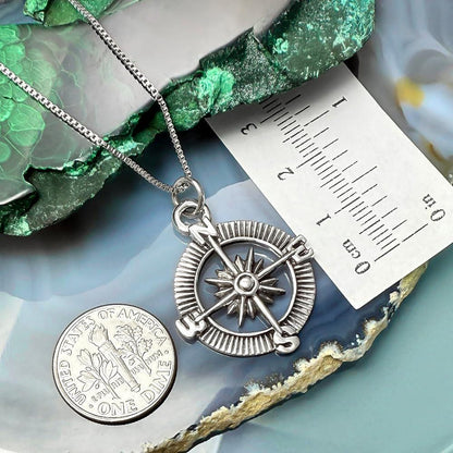 a silver compass pendant hanging from a chain, with a United States quarter coin placed next to it.