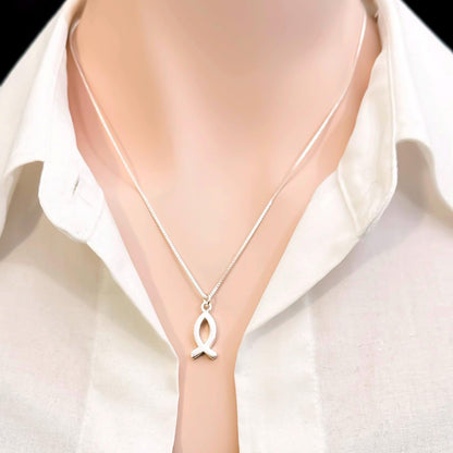 A silver necklace with a pendant is worn around a person's neck.