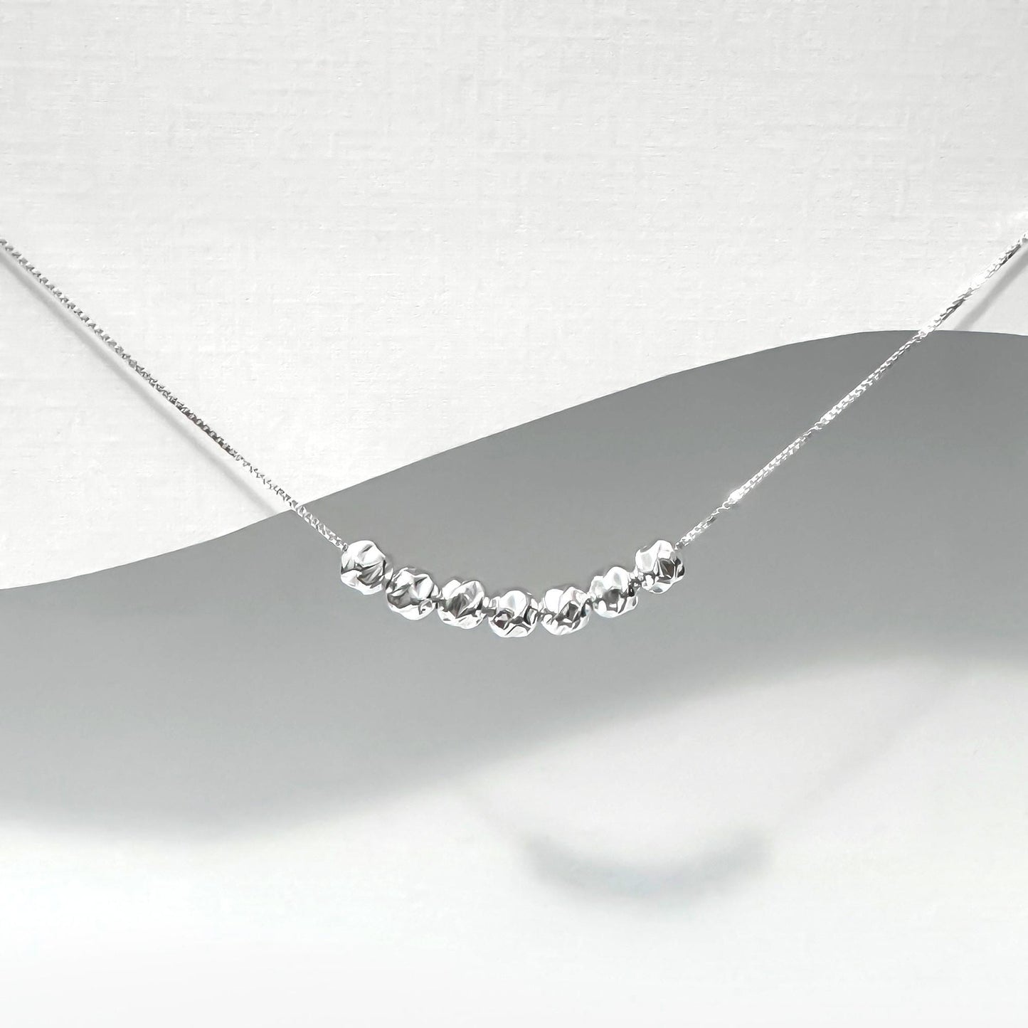 A silver necklace with a row of small, shiny beads or stones on a chain.