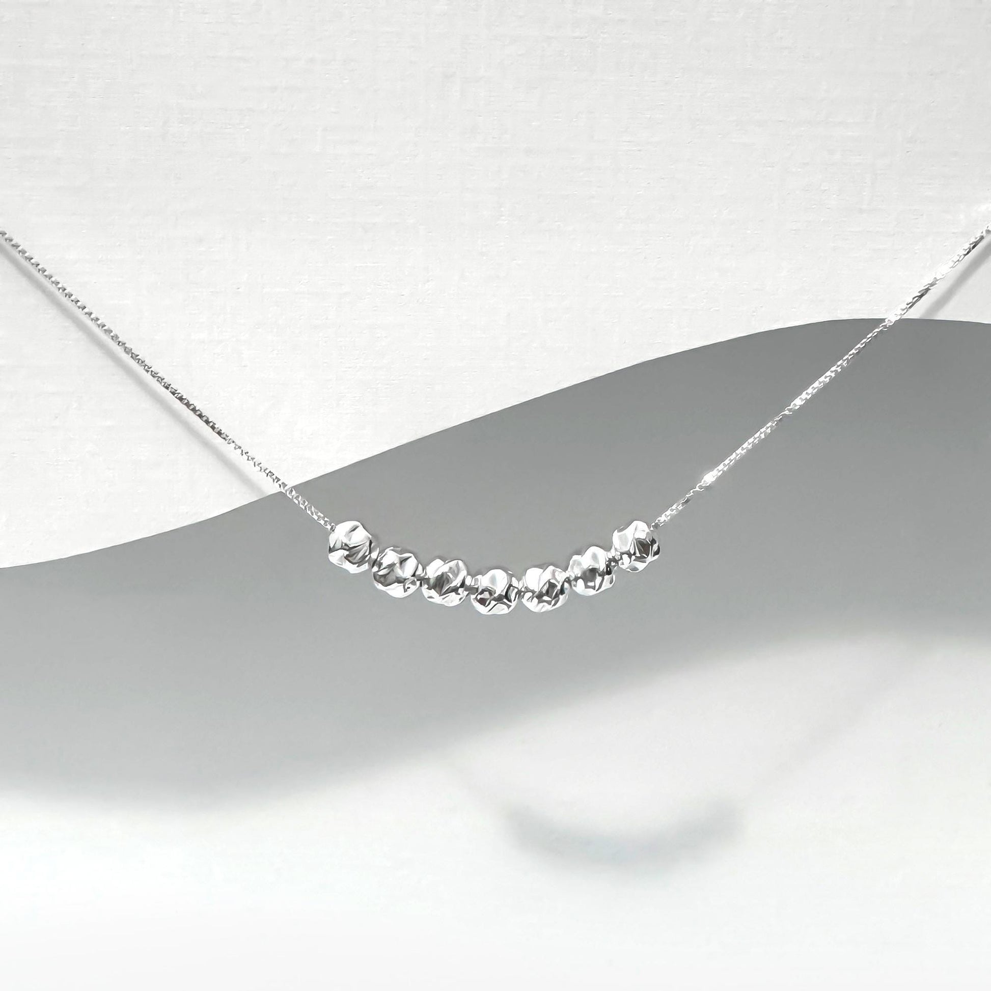 A silver necklace with a row of small, shiny beads or stones on a chain.