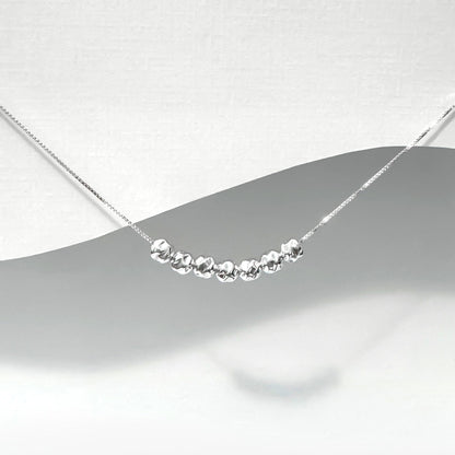 A silver necklace with a row of small, shiny beads or stones on a chain.