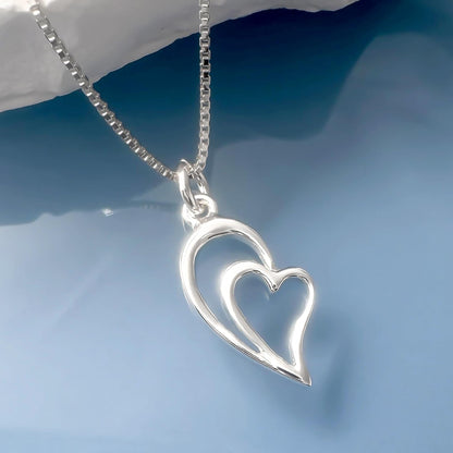A silver heart-shaped pendant with a chain is displayed against a blue background.