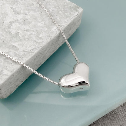 A silver heart-shaped pendant necklace is displayed on a white stone surface.