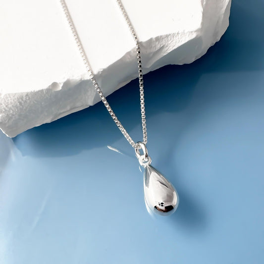 A silver necklace with a pendant is displayed against a blue background.