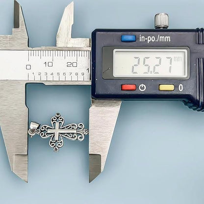 A silver cross pendant is being measured with a caliper, which displays the size in millimeters.