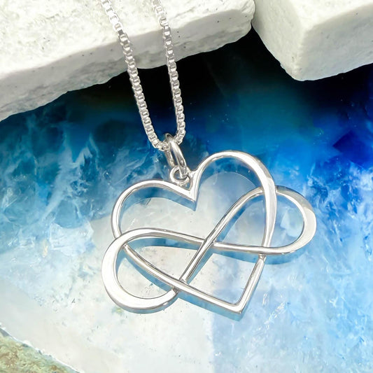 A silver heart-shaped pendant with an infinity symbol is displayed against a blue and white background.