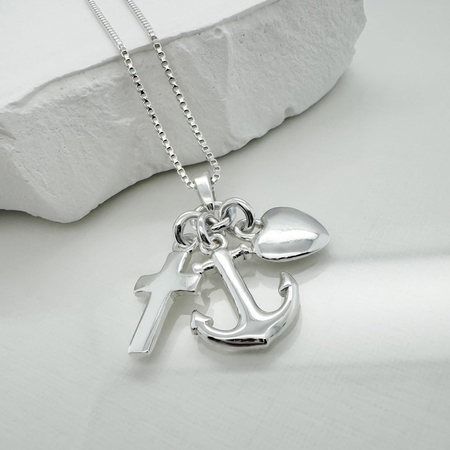 A silver necklace with a pendant featuring a cross, an anchor, and a heart charm.