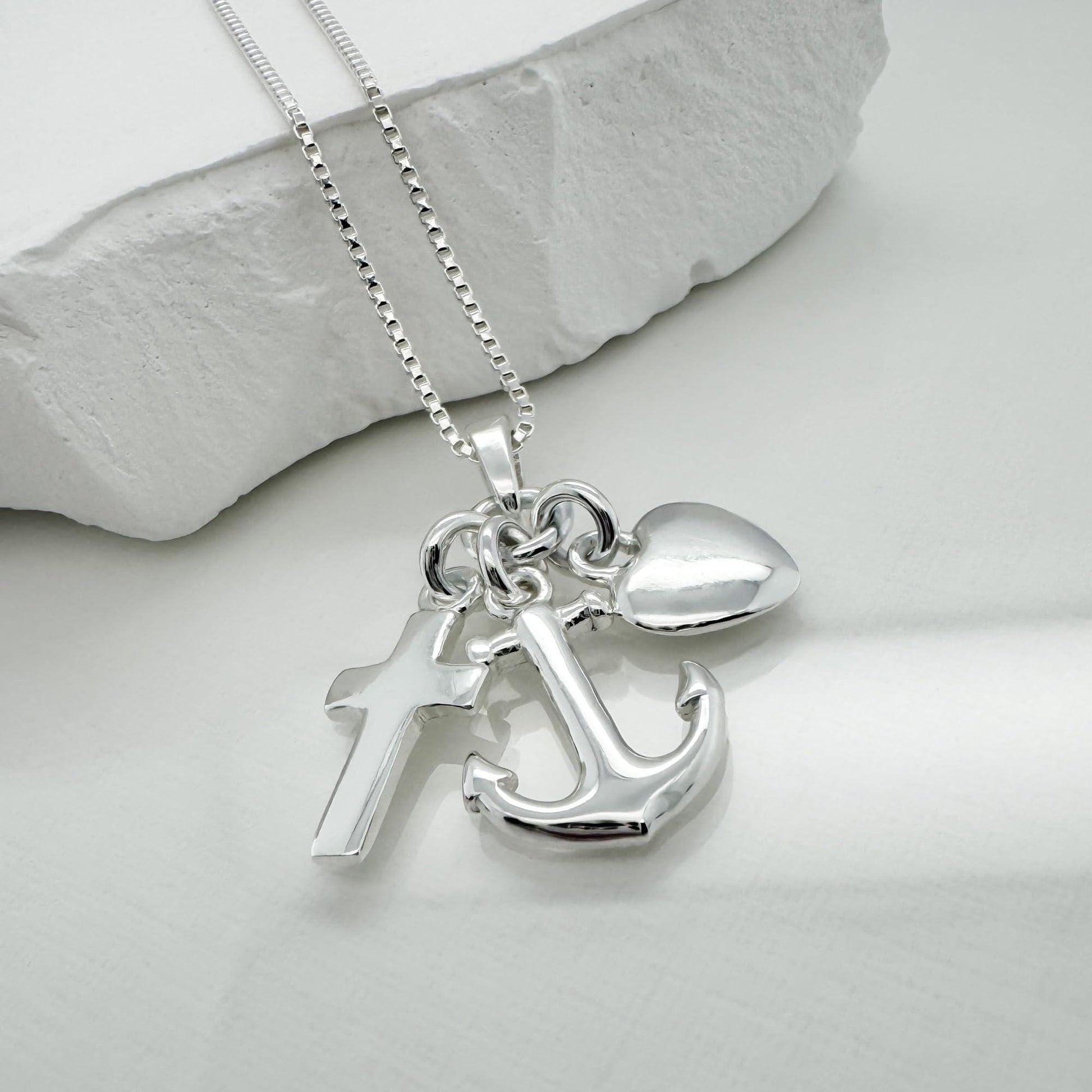 A silver necklace with a pendant featuring a cross, an anchor, and a heart charm.