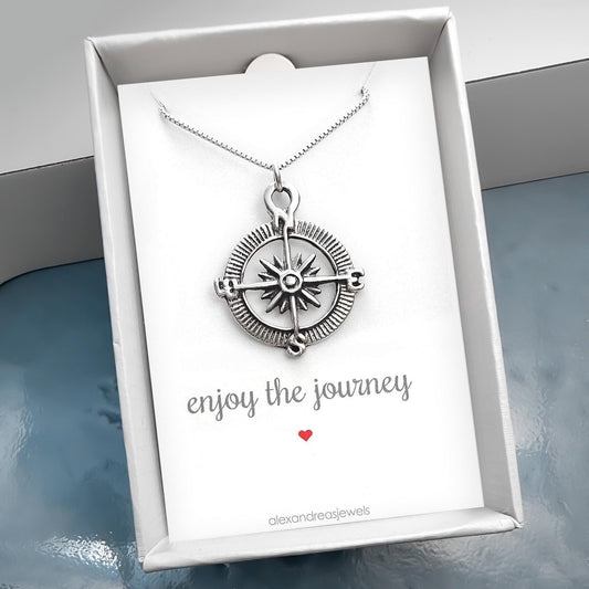A silver compass pendant is displayed in a white box with a message encouraging the enjoyment of the journey.
