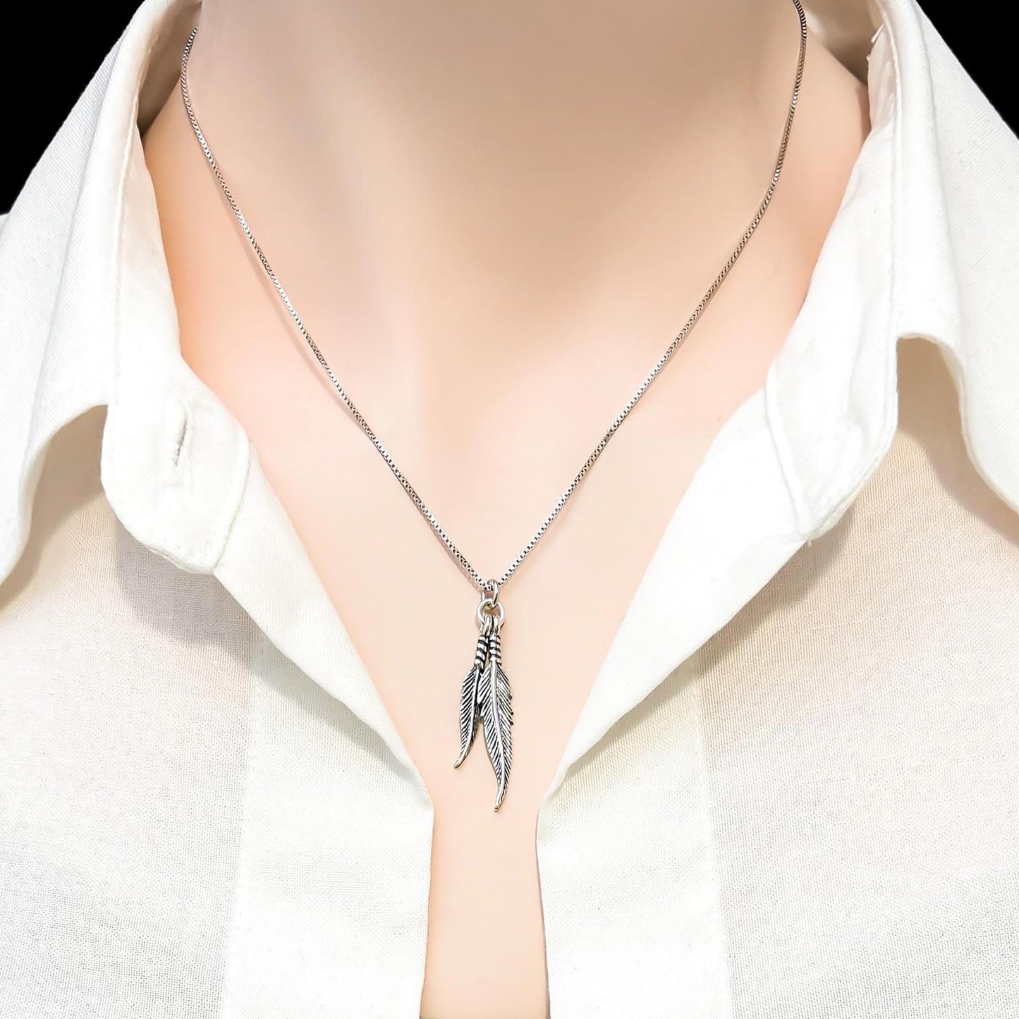 A silver necklace with a pendant featuring two feathers is displayed on a mannequin's neck.