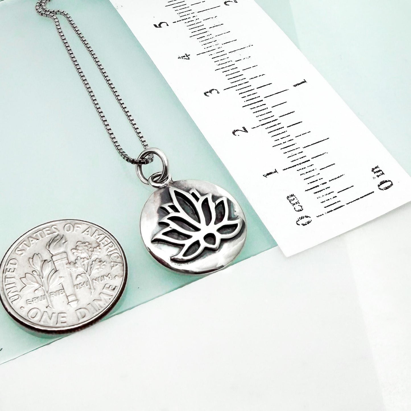 a silver necklace with a pendant, a United States one dollar coin, and a ruler for size comparison.