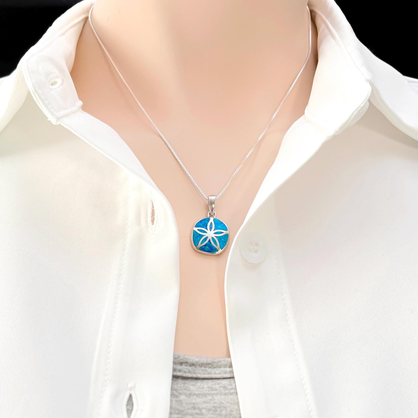 A close-up view of a person wearing a white shirt and a necklace with a blue pendant.