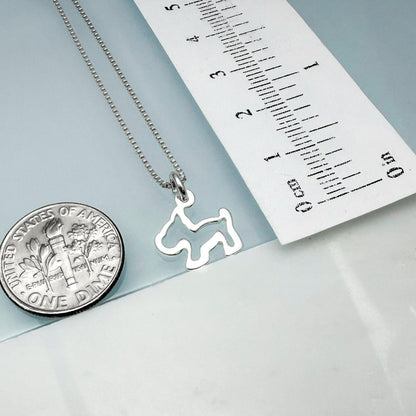 a silver dog-shaped pendant hanging from a chain, placed next to a United States one-dollar coin for scale.
