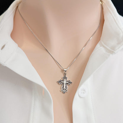 A silver cross pendant necklace is worn around a person's neck, with a white collared shirt visible underneath.