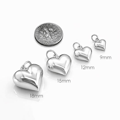 a collection of five silver heart-shaped charms, each varying in size, with a United States one dollar coin placed next to them.