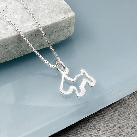 A silver necklace with a pendant in the shape of a dog silhouette is displayed on a light blue surface.