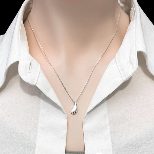A close-up view of a person wearing a white collared shirt and a silver necklace with a pendant.