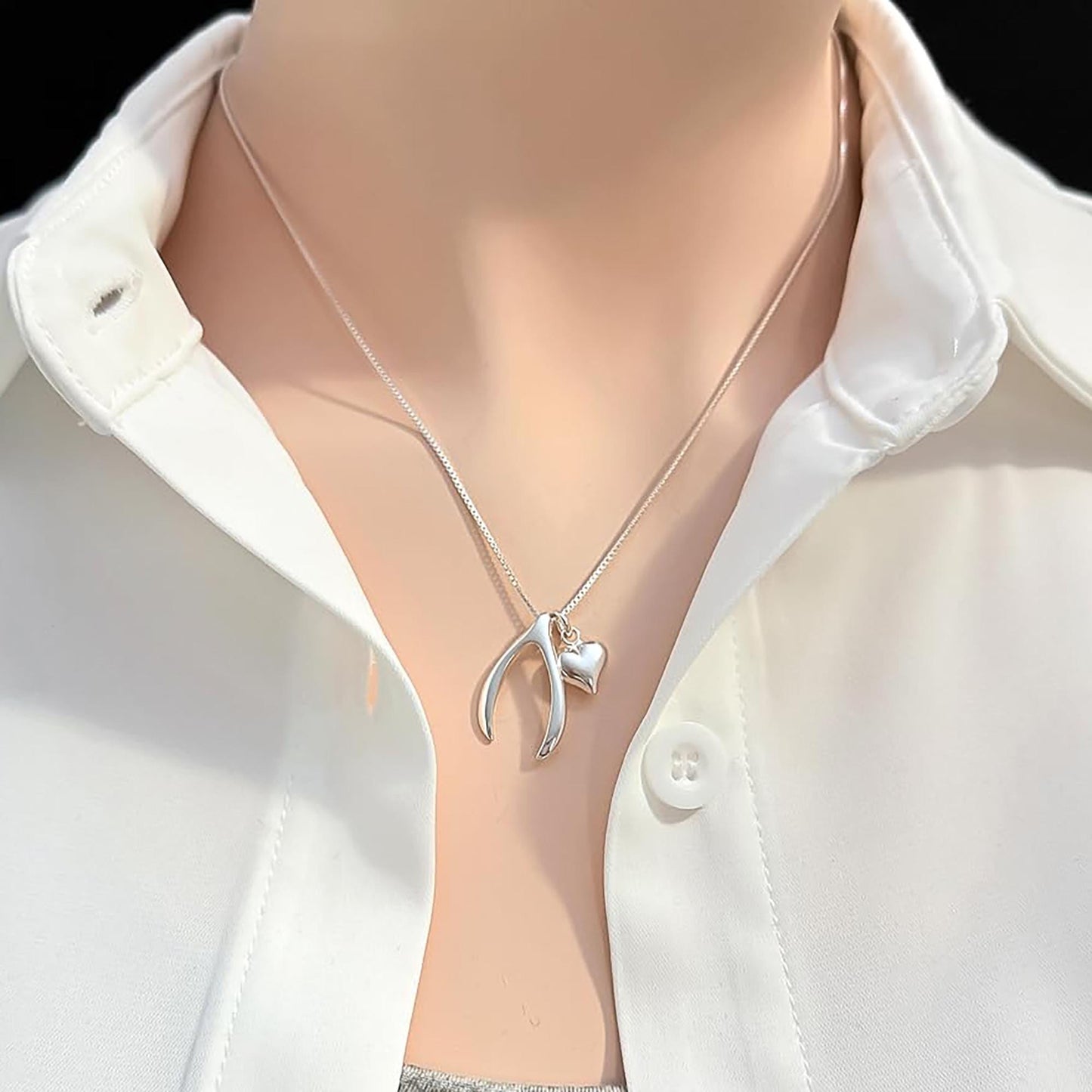 A silver necklace with a heart-shaped pendant is worn around a person's neck, who is wearing a white collared shirt.