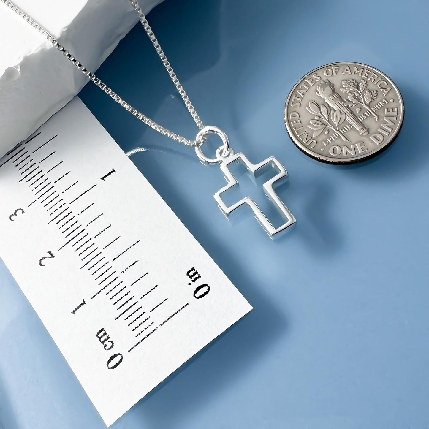 a silver cross pendant on a chain, placed next to a United States one dollar coin.