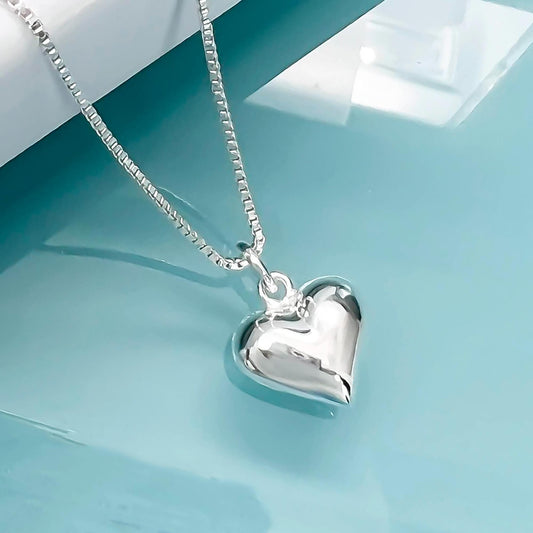 A silver heart-shaped pendant necklace with a chain is displayed against a blue background.