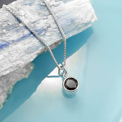 A silver necklace with a round black gemstone pendant is displayed against a blue background.