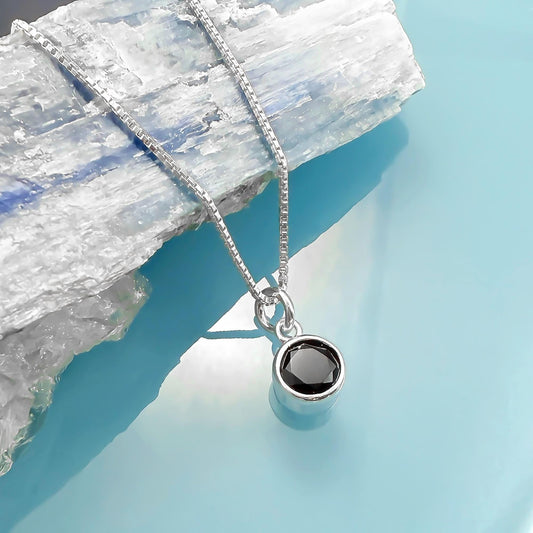 A silver necklace with a round black gemstone pendant is displayed against a blue background.