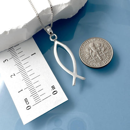 a silver fish pendant necklace and a United States one dollar coin placed on a blue surface.